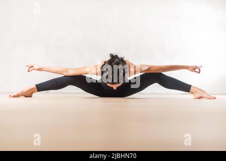 Young Caucasian dancer doing seated wide leg forward bend exercise stretching spine and legs. Stock Photo