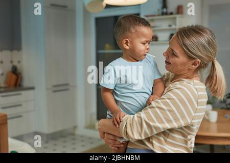 Portrait of happy Caucasian mother holding cute toddler boy in home kitchen interior, copy space Stock Photo