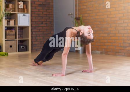Woman doing yoga exercise standing in Table Top Pose Ardha Purvottanasana on floor at home. Stock Photo