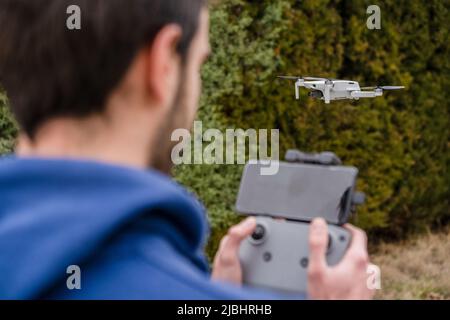 Close-up of a young man with remote control operating flying drone outdoors with trees behind Stock Photo