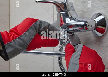 Replacing a worn out shower valve switch. Plumber's hands in work gloves with an adjustable wrench Stock Photo