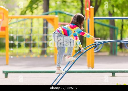 a girl in a bright striped jumper and jeans, climbs the childrens stairs on the playground Stock Photo