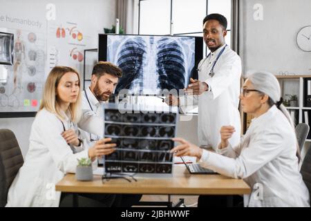 Qualified international doctors of differents ages gathering at boardroom for examining x ray scan of lungs and brain. Medical specialists thinking about diagnosis and treatment of severe patient. Stock Photo
