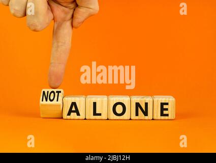 You are not alone symbol. Businessman turns wooden cubes and changes concept words alone to not alone. Beautiful orange background. Business, support Stock Photo