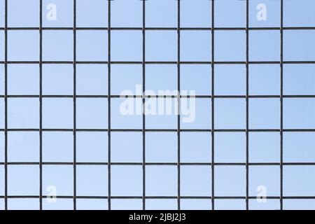 Close-up of a fence whose wire forms perfect squares, with the blue sky in the background Stock Photo