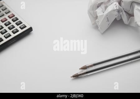 Image from above of a table on which there is a calculator, a crumpled paper, and pens with copy space in the center Stock Photo