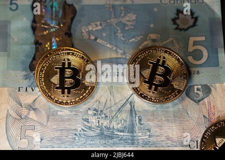 Toronto, Canada - October 30. 2021: Bitcoin coins on top of Canadian Dollar Banknotes, trading BTC with CAD Stock Photo