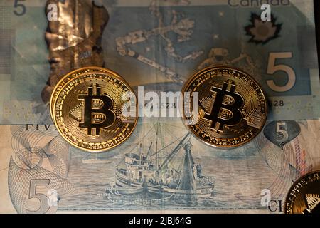 Toronto, Canada - October 30. 2021: Bitcoin on five Canadian Dollar banknotes. CAD bills and gold Bitcoin coins. Trading cryptocurrency in Canada conc Stock Photo