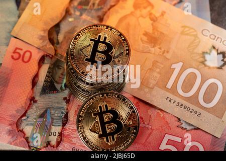 Toronto, Canada - October 30. 2021: Bitcoin on fifty and one hundred Canadian Dollar banknotes. Cryptocurrency trading with Canadian money Stock Photo