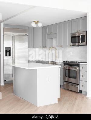 A grey kitchen with stainless steel appliances, gold faucet, white marble countertops, and a subway tile backsplash. Stock Photo