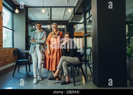 Multiethnic entrepreneurs smiling at the camera in a boardroom. Group of successful businesswomen working as a team in an inclusive workplace. Diverse Stock Photo