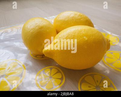 Washed lemons on top of a plastic food storage bag on a light wood table Stock Photo
