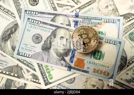 Bitcoin piled up on dollar banknotes. Gold coins on top of one hundred dollar bills. Spread out banknotes as background. Stock Photo