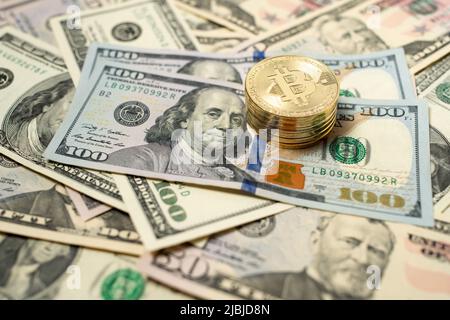 Bitcoin piled up on dollar banknotes. Gold coins on top of one hundred dollar bills. Spread out banknotes as background. Stock Photo