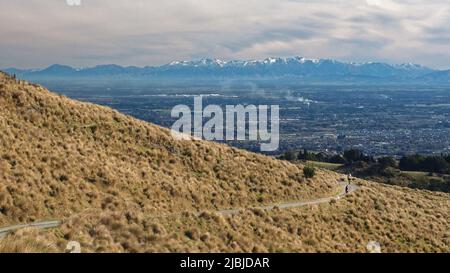 Cyclists riding on a track in the Port Hills Christchurch with a view over the Canterbury Plains to the Southern Alps NZ Stock Photo