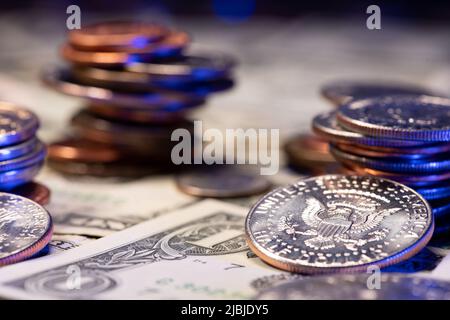 Half dollar coin with eagle, next to piled up us dollar coins towering over 1 usd bills. Dollar banknotes as background. Economy and prosperity in the Stock Photo