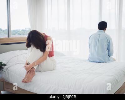 The anxiety of Asian couple lovers on the bed. Sad young woman and man sitting on the bed with relationship difficulties feeling sad and thinking in t Stock Photo