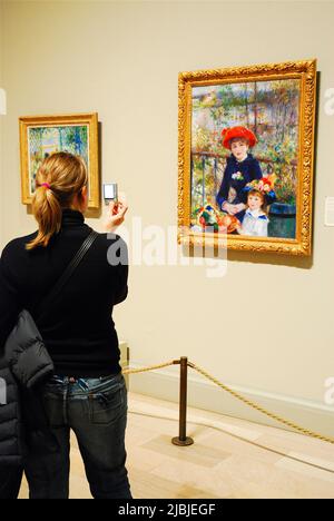 A young adult woman captures a photo of Renoir's Two Sisters on the Terrace on her flip phone while visiting the Chicago Art Institute