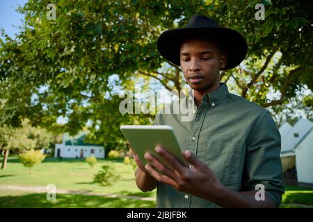 Mixed race male farmer typing on digital tablet standing outdoors in green fields Stock Photo