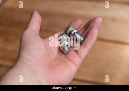 Bolts and nuts lie in the palm of my hand. Two silver bolts with screwed-on nuts lie in the hand of a middle-aged man. A first-person view. Selective Stock Photo