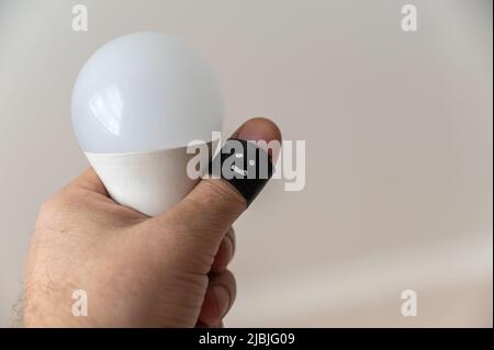 A middle-aged man holds a white LED light bulb in his hand. The phalanx of his thumb is wrapped with black electrical tape. A happy, smiling face is p Stock Photo