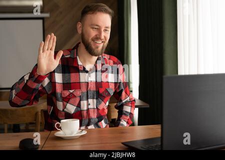 Smiling millennial Caucasian casual man, smiling while working with apps, guy chatting online on laptop, sitting at table in cafe, happy 30 year old Stock Photo