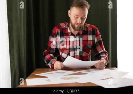Serious thoughtful businessman looking at papers while sitting at table and working at home or office interior. Business or freelancing Stock Photo