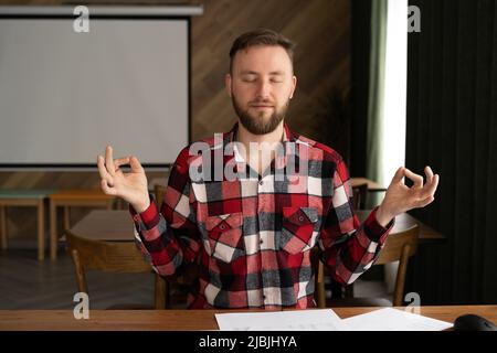 Handsome male businessman meditates while sitting in a cozy office, meditation and relaxation from hard work, entrepreneur resting Stock Photo