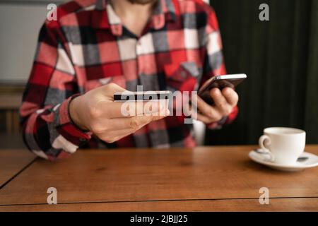 Close-up, male hands hold a credit card and a smartphone, a man pays online, uses banking services, enters information while shopping, orders online Stock Photo