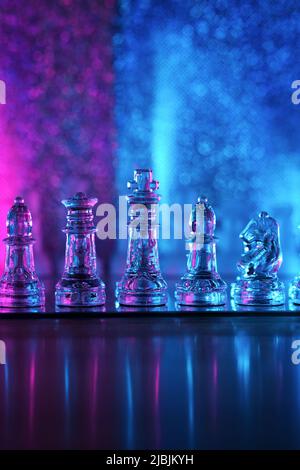 Transparent glass chess pieces. Queen, King, White-field and black-field Bishop, Knight on translucent chessboard. Cold colored illuminated shiny back Stock Photo