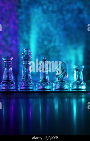 Transparent glass chess pieces. Queen, King, Bishop, Knight and Rook on translucent chessboard. Cold colored illuminated shiny background. Reflection. Stock Photo