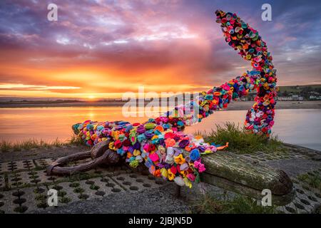 Appledore, North Devon, England. Tuesday 7th June 2022. The sun rises behind the landmark anchor on the quay in Appledore. The anchor has been decorated with hundreds of colourful crocheted flowers by the residents of the North Devon coastal village. Credit: Terry Mathews/Alamy Live News Stock Photo