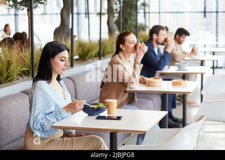 Group of people sitting in row at food court in shopping mall cafe area, copy space Stock Photo