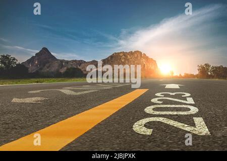 2023 new year 2023 or beginning of 2023 word concept written on a road in the middle of a country road with mountains sunset concept backdrop. Stock Photo