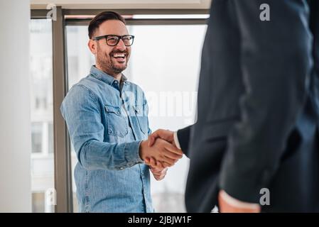 Happy business partners shaking hands in meeting. Entrepreneurs congratulating over successful deal. They are standing in corporate office. Stock Photo