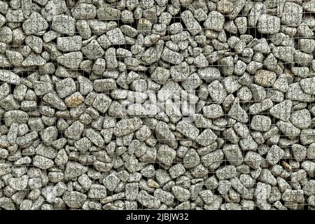 Textured background of a stone wall with iron netting. Stone wall in wire frame. Stock Photo