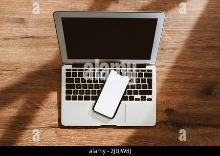 Mobile phone with blank white mockup touchscreen and laptop computer on office desk, top view flat lay with copy space for business communication and Stock Photo