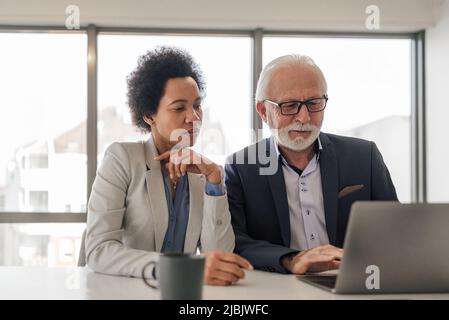 Focused male and female partners analyzing business plan on laptop. Professionals working on strategy during meeting. They are sitting at desk in offi Stock Photo