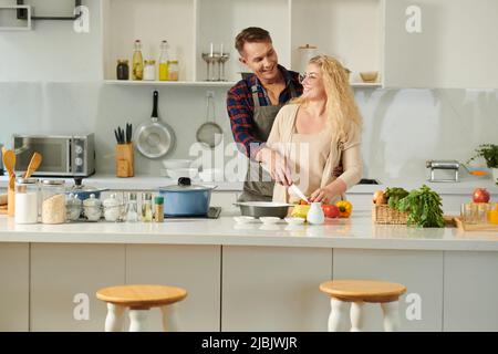 Joyful couple enjoying romantic date in kitchen, they are flirting and cooking dinner Stock Photo