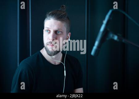 Portrait of a caucasian bearded musician in headphones in a black recording studio with a microphone Stock Photo