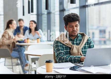 Portrait of modern business person working with laptop at cafe table in food court, copy space Stock Photo
