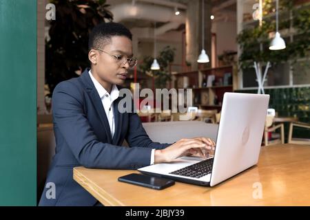 Young business woman working is a cafe with a laptop, African-American is focused on the end of the project, the deadline is for lunch break Stock Photo