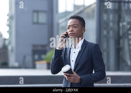 Business woman in business attire talking on the phone, African American woman on a break with a cup of hot drink walks in the business district near Stock Photo