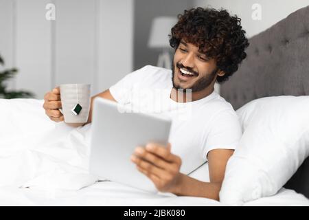 Cheerful indian man drinking tea and using digital tablet Stock Photo