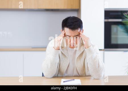 Thoughtful serious young asian man looking away. student writer sit at home office desk with laptop thinking of inspiration search solution ideas lost Stock Photo