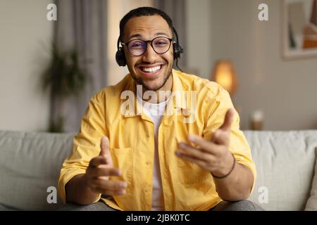 Smiling young African American man in headset chatting online, having webinar or video conference at home office Stock Photo