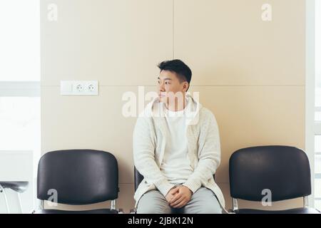 young asian man waiting for an interview or meeting sitting in the hallway in the waiting room. Student or entrant in the reception for exam or employ Stock Photo