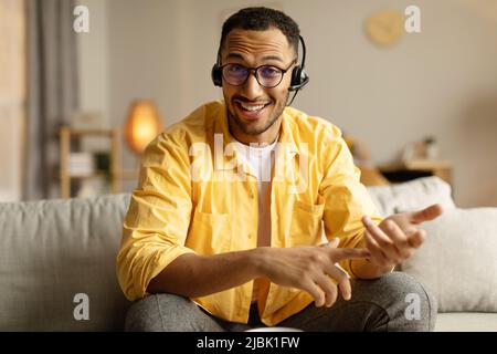 Young black man in headphones having video call or business conference, smiling at webcam, chatting online from home Stock Photo