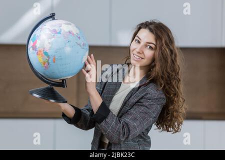 Portrait of young beautiful woman, travel agent, holding globe, looking at camera, smiling Stock Photo