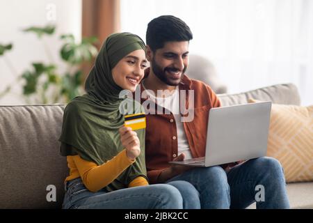 Middle Eastern Spouses Shopping Online Via Laptop Holding Card Indoor Stock Photo